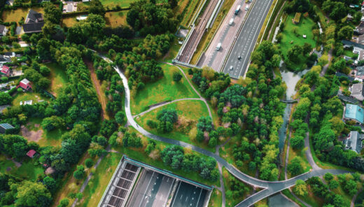 Directly above drone view of green bridge with public park crossing above semi underground highway in the Netherlands.